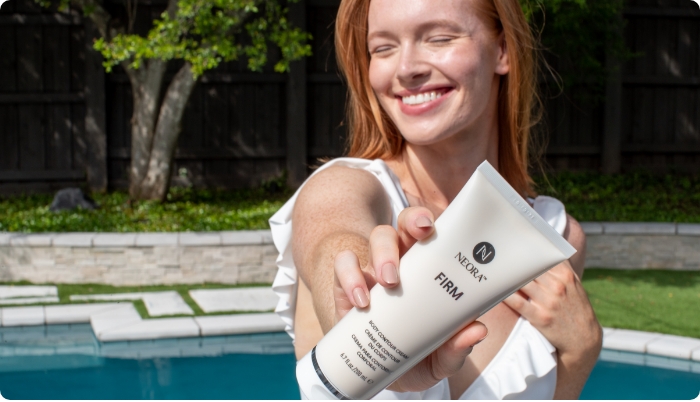 Image of woman by the pool smiling and holding Neora’s Firm Body Contour Cream in front of her